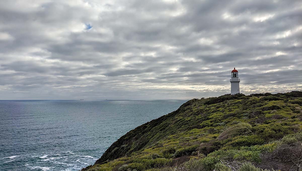 Cape Schanck Lighthouse, standing over calm ocean waters with an overcast sky behind